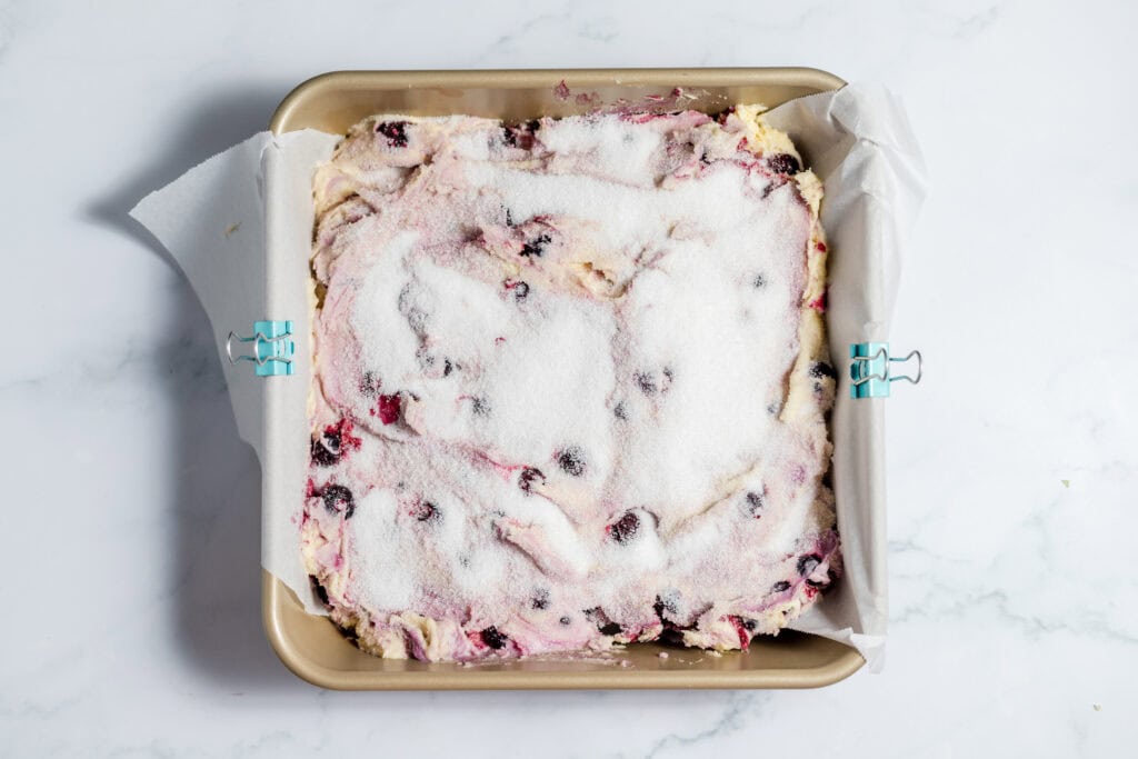 Blueberry coffee cake in a baking dish. The dish is lined with parchment paper and there is a lot of sugar on top. 
