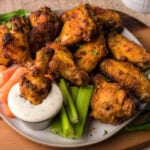 Air fried chicken wings on a plate with some veggies and dip.