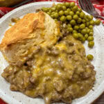 Ground beef casserole with biscuits on a plate with English peas.