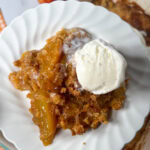 Peach dump cake on a white plate with a scoop of ice cream on top.