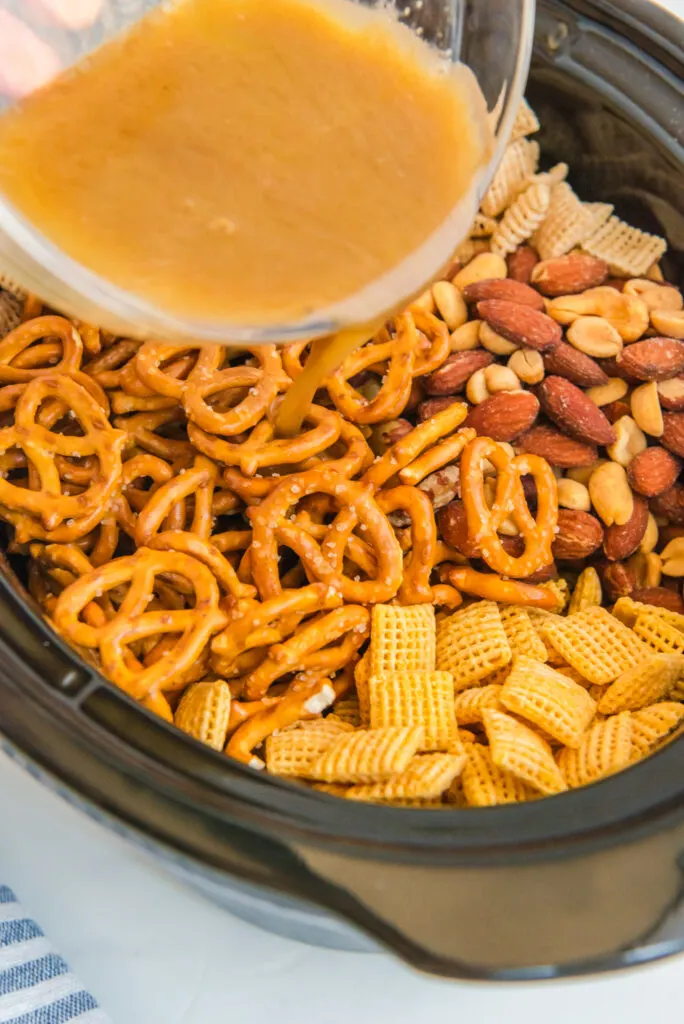 Pouring a butter mixture over the top of chex mix.