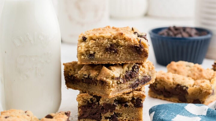Chocolate chip cookie bars stacked on top of each other next to a glass of milk.