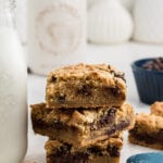Chocolate chip cookie bars stacked on top of each other. They are next to a glass of milk.