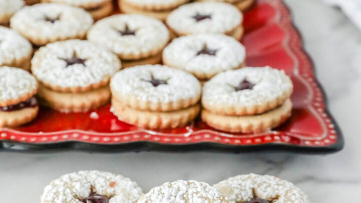 Linzer cookies on a red plate. There are some on the counter.