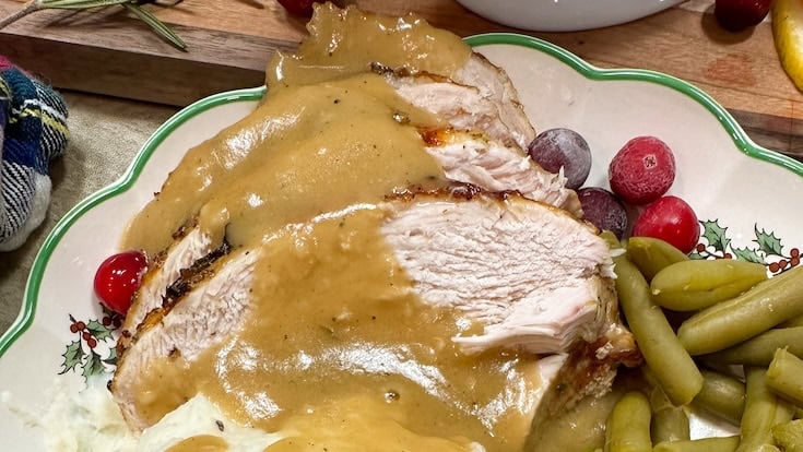 Sliced turkey breast with brown gravy on a holiday plate, served with green beans, mashed potatoes, and garnished with whole cranberries—made easy with our Slow Cooker Turkey Breast Recipe for juicy, tender turkey with minimal prep.