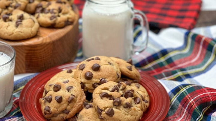Chocolate chip cookies on a red plate. The cookies are stacked on each other. There is a glass of milk in the background.