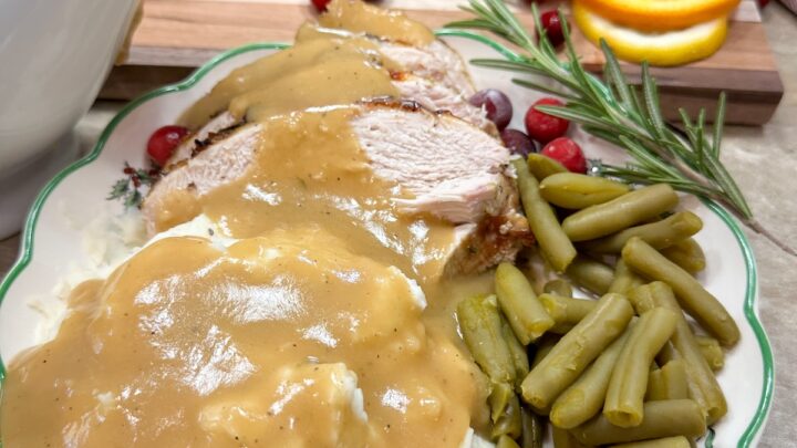 Brown gravy drizzled over mashed potatoes and turkey. There are some green beans on the plate.