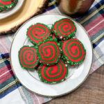 Red and green pinwheel cookies on a white plate. There is a coffee cup in the background.