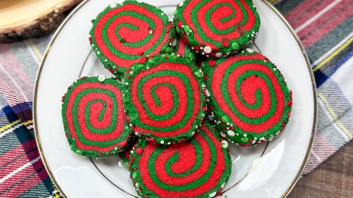 Red and green pinwheel cookies on a white plate. There is a coffee cup in the background.