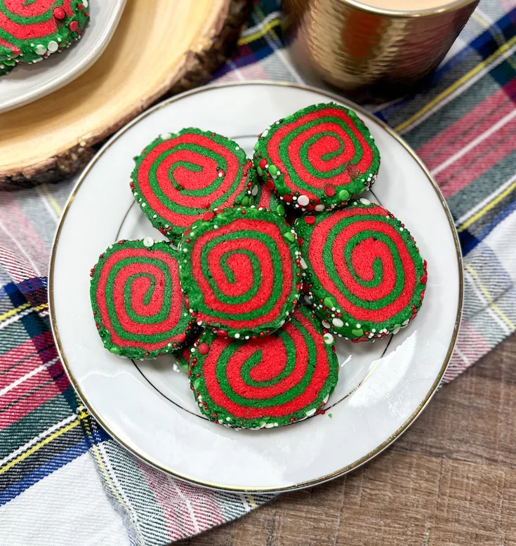 Red and green pinwheel cookies on a white plate. There is a coffee cup in the background.