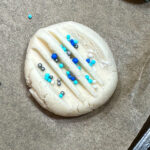 Sprinkles on an uncooked shortbread cookie.