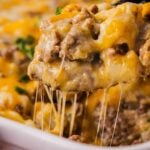 Beefy casserole on a black spoon with potatoes and melted cheese.