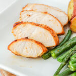 Turkey tenderloin slices on a white plate next to green beans.