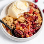 apple crisp in a white bowl. There is a spoon in the bowl and some ice cream on top.