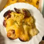 Potato sausage and casserole with cheese on a white plate.