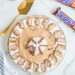 no bake snickers bar pie on a counter next to two snickers candy bars