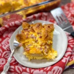 egg casserole on a white plate next to a casserole dish. There is a fork on the plate.