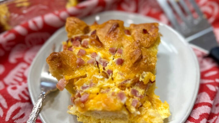 egg casserole on a white plate next to a casserole dish. There is a fork on the plate.