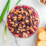 Cream cheese dip in a glass bowl topped with pecans.
