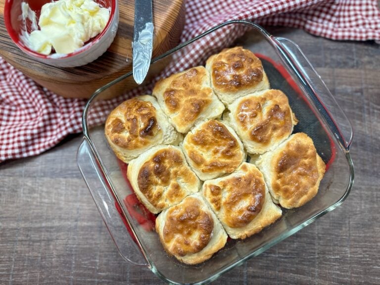 Nine biscuits in a baking dish next to a knife and butter.