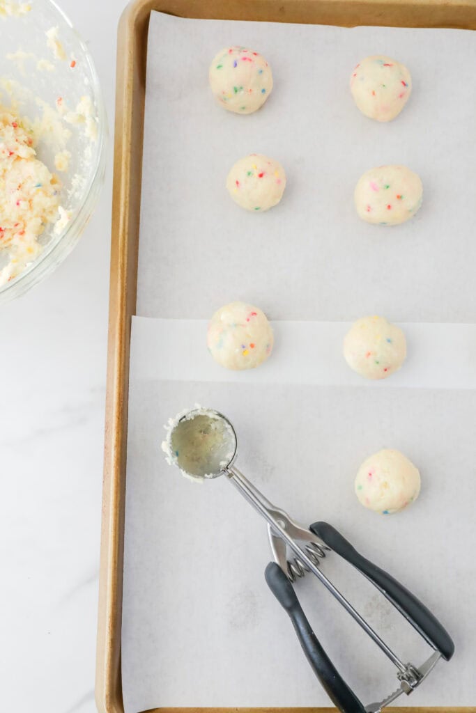 Scoops of dough on a cookie sheet lined with parchment paper.