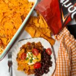 Dorito casserole recipe with beans on a white plate next to a bag of Doritos.