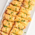 Slices of Sloppy Joe French Bread topped with melty Colby Jack cheese and garnished with fresh parsley, displayed on a white platter.