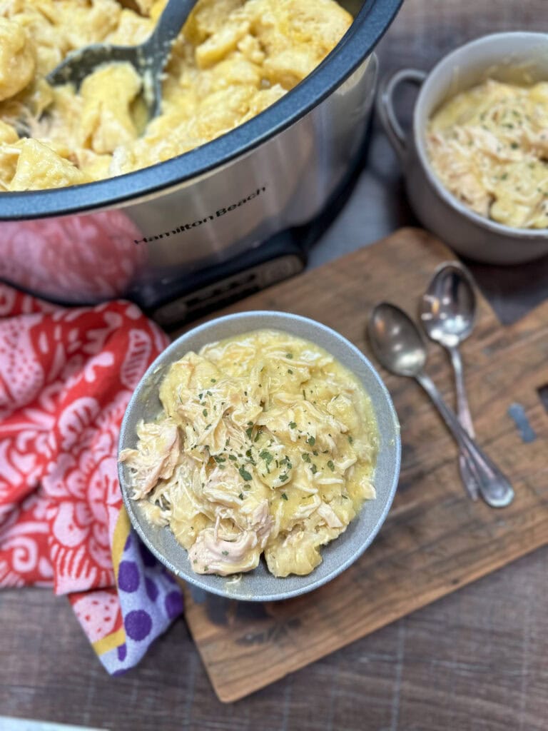 Chicken and dumplings in a bowl next to a crock pot.