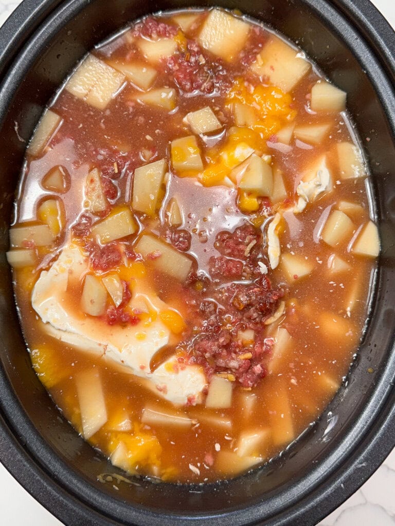 Chicken broth in a crock pot with ingredients for soup.