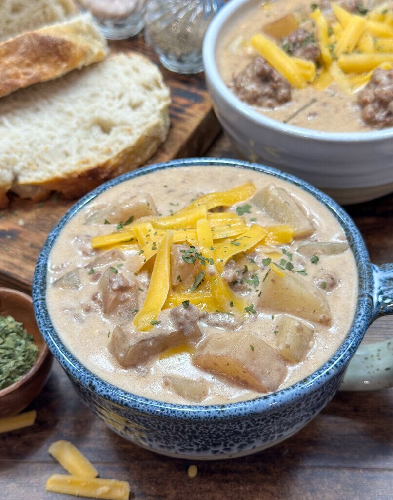 Crock Pot cheeseburger soup in a blue-rimmed bowl. There is some sliced sourdough bread next to the bowl.