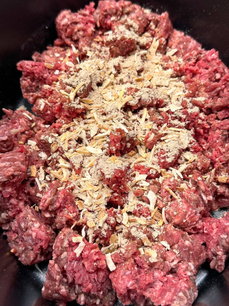 Ground beef in a slow cooker. Onion soup mix is sprinkled on top of the meat. 