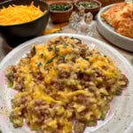 Ground beef with rice casserole on a plate. There is some shredded cheese and biscuits in the background.