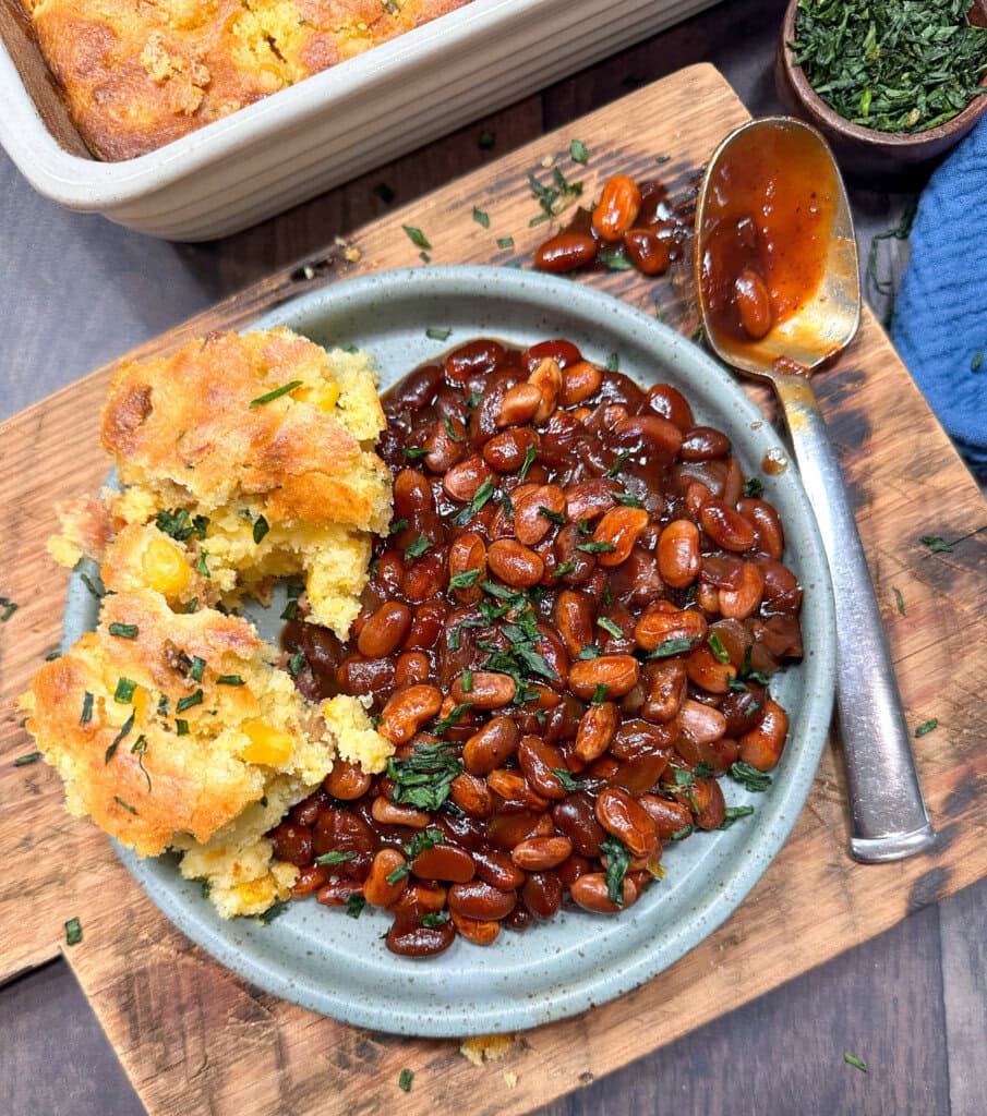 BBQ baked beans on a plate with some cornbread and a spoon.