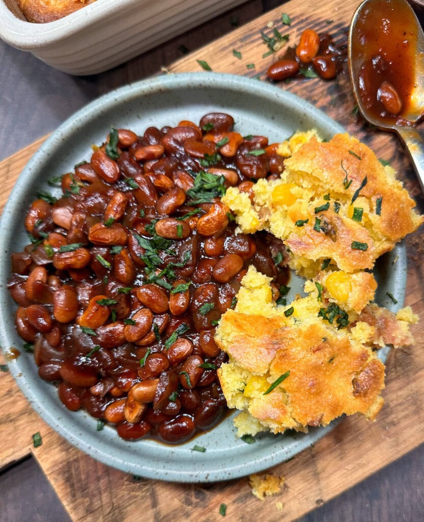 Baked beans on a plate with some cornbread. 