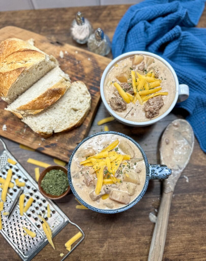 slow cooker cheeseburger soup in a couple of soup bowls. There is some bread next to the bowl on a cutting board.