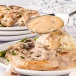 Pork chops and gravy on a plate. There is a spoon with gravy over the pork chops.