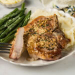 Garlic butter pork chops on a plate with mashed potatoes and green beans.