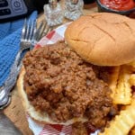sloppy joe meat on a bun next to some french fries.