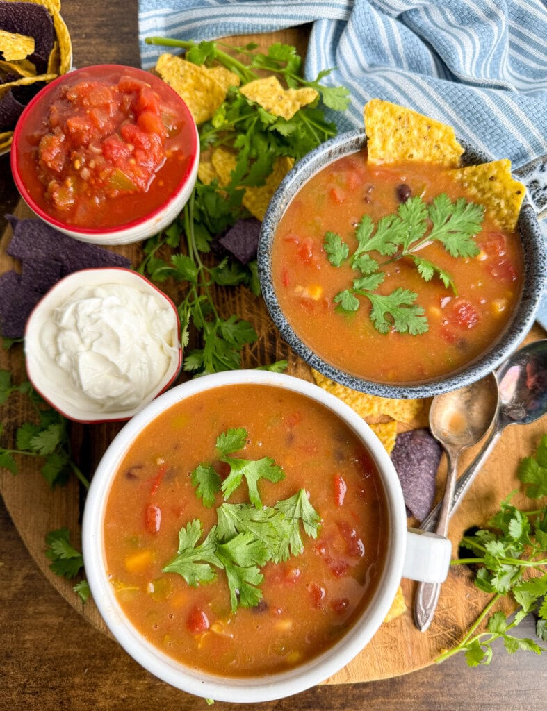 Two bean soups on a cutting board. There is some sour cream and salsa next to the soups.