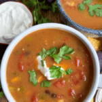 Bean soup on a cutting board in a white bowl. There's some sour cream and cilantro on top.