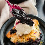 Pouring blueberry sauce on top of ice cream on blueberry cobbler.