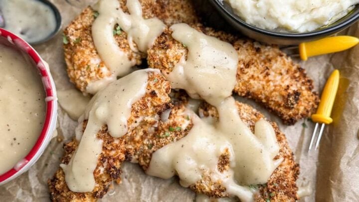 Air fryer chicken strips on a cooking sheet covered in gravy.