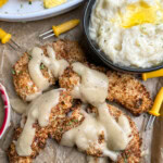 Chicken strips covered in gravy with mashed potatoes an dcorn on the side.