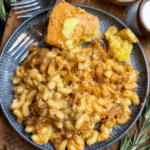 A plate of pulled pork BBQ mac and cheese served with buttered cornbread sits on a wooden tray, garnished with rosemary. Text reads: 30-Minute Pulled Pork BBQ Mac and Cheese. Pin it now and make it today!.