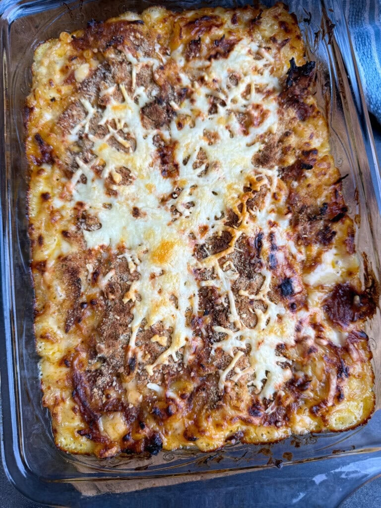 A baked casserole dish filled with macaroni and pork, topped with melted cheese and browned bits, sits on a countertop.