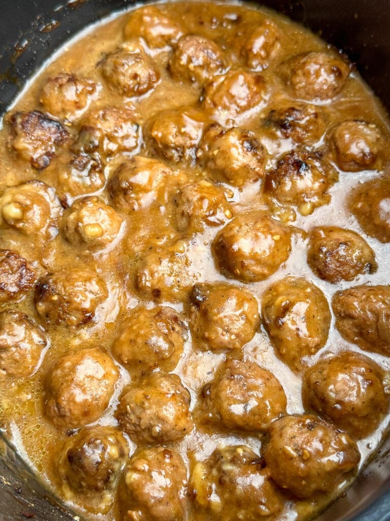 Close-up of a pot filled with meatballs simmering in a thick, brown gravy sauce. The meatballs are evenly coated and appear tender and juicy.