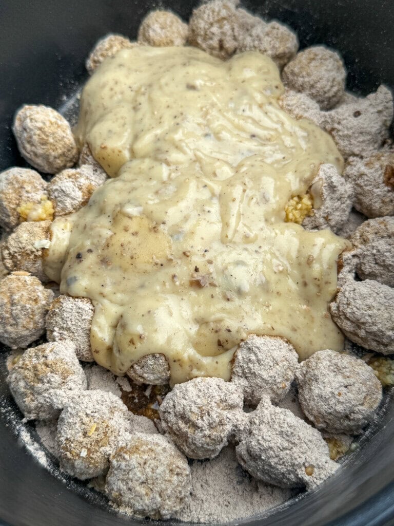 Raw meatballs coated in gravy and onion soup mix are arranged in a pot, topped with a cream of condensed mushroom soup in a crock.