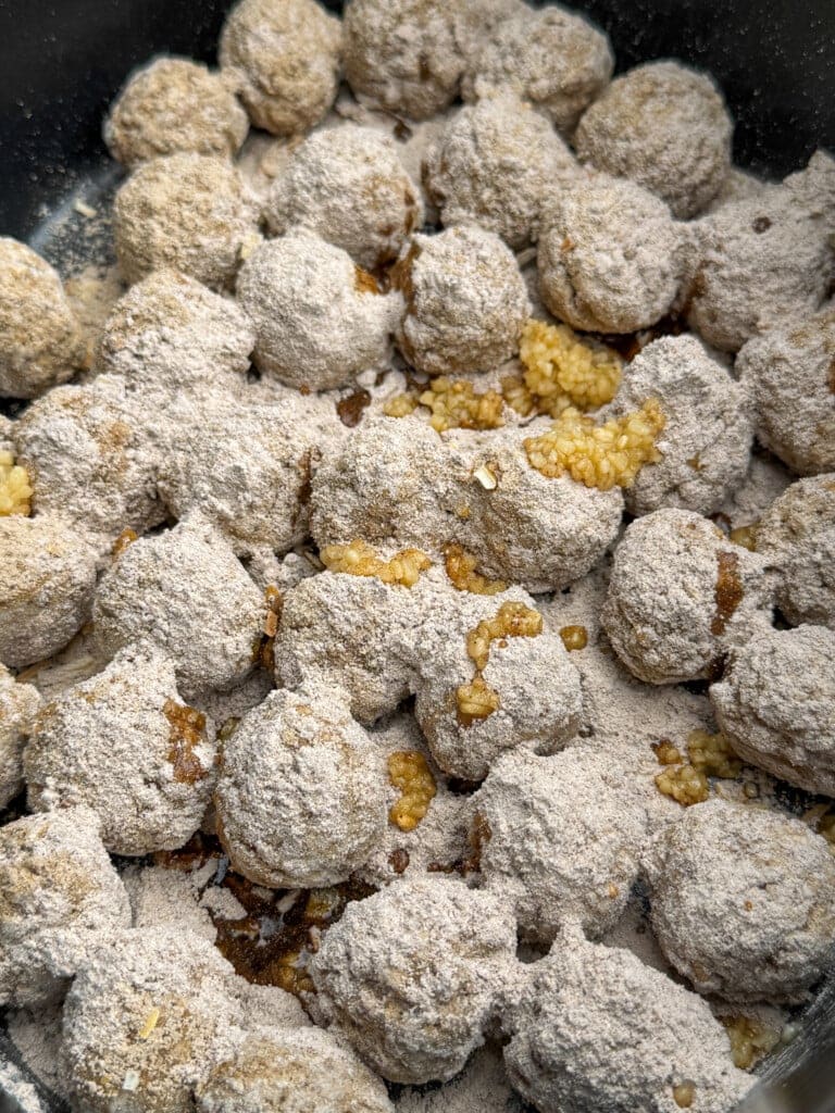A close-up of numerous round meatballs coated in a dry gravy and onion soup mix. Minced garlic is scattered among the meatballs. 