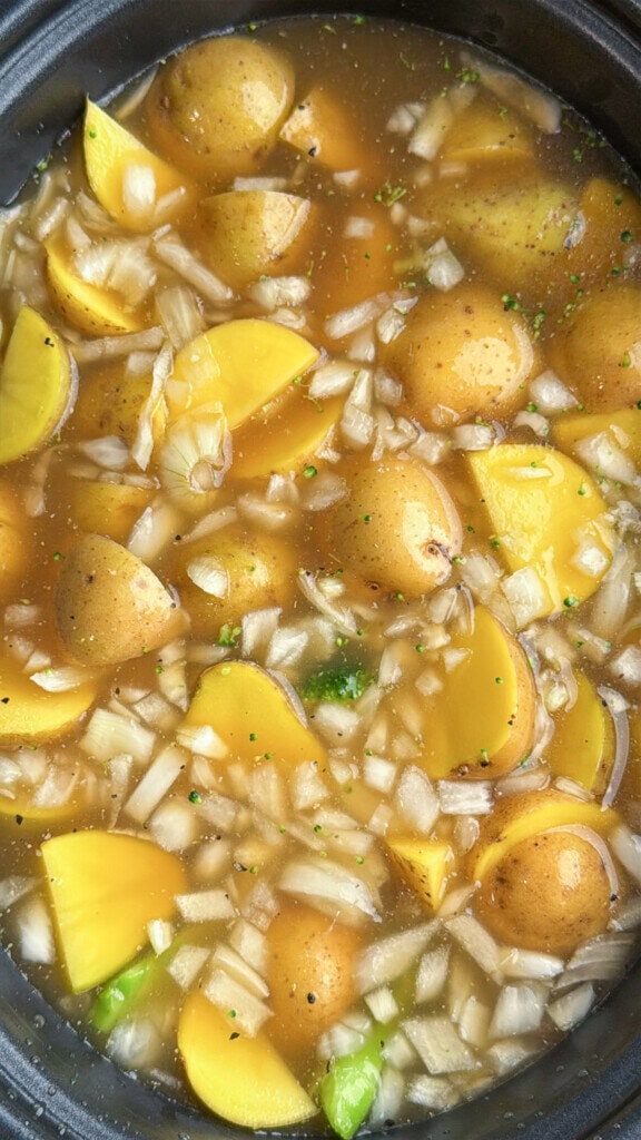 Yellow potato wedges, chopped onions, and broccoli are simmering in a pot of broth, creating a hearty soup or stew.