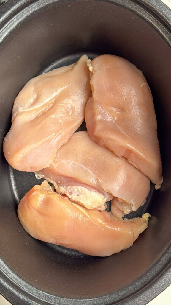 Four raw chicken breasts placed in a black cooking pot, ready to be prepared or cooked.